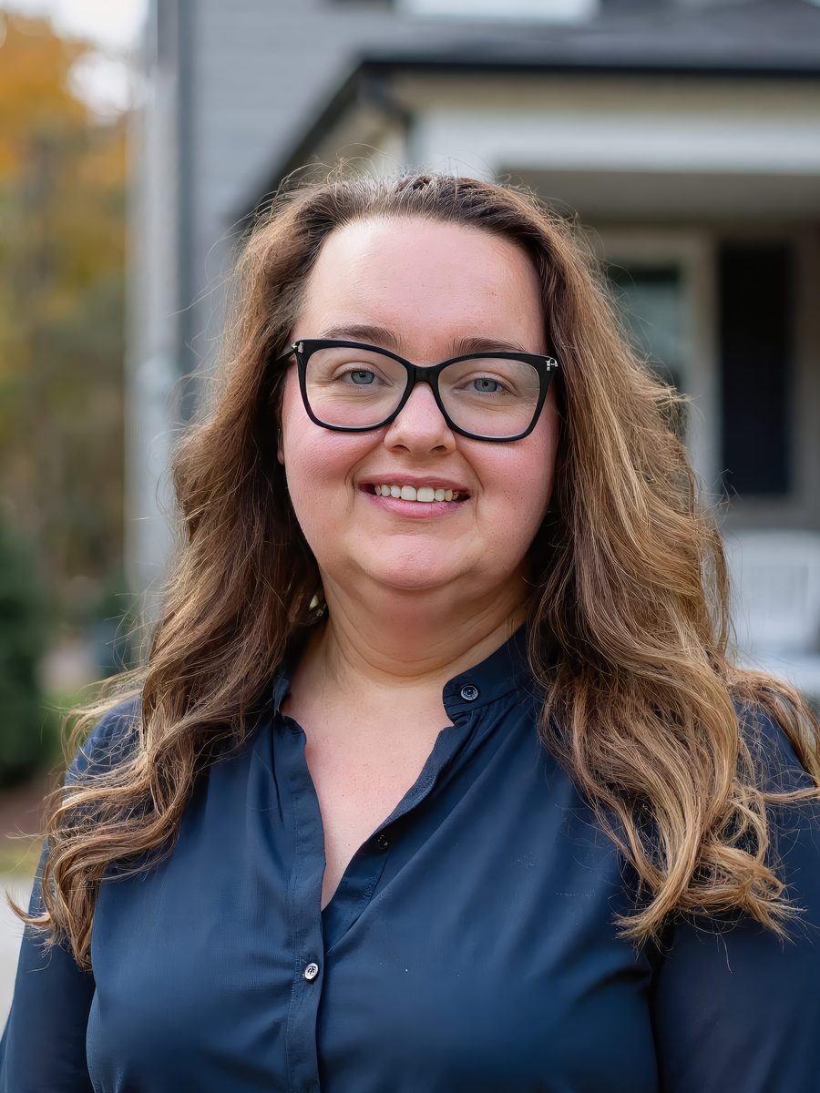 Catherine Mason, RE/MAX Rise real estate advisor, smiling outdoors in a navy blouse in front of a gray house